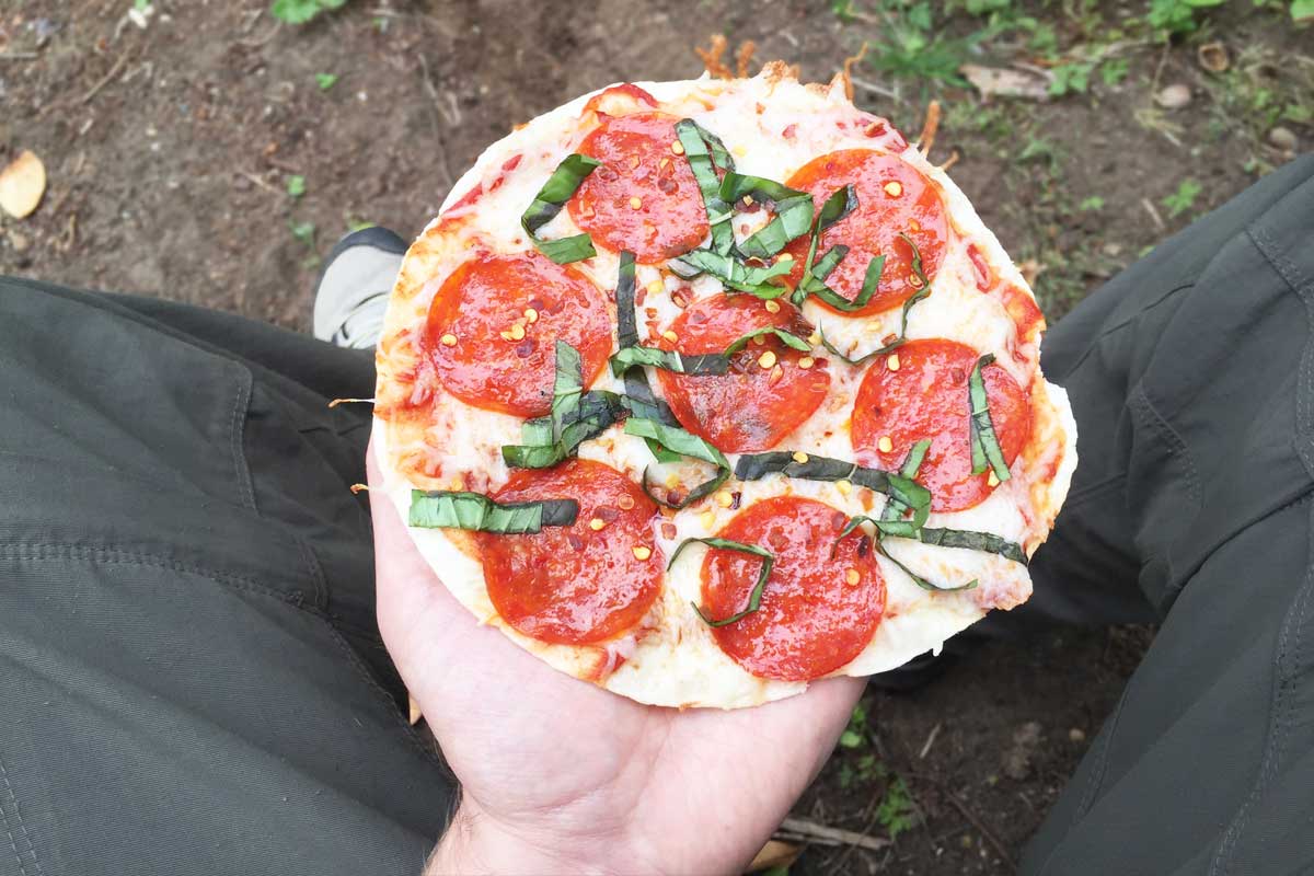 Camper pov holding fresh made torilla trail pizza.