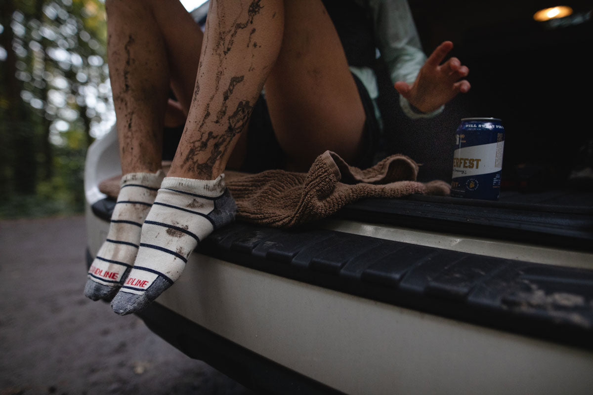 Trail runner resting in the trunk of a car post run with muddy socks and shoes.