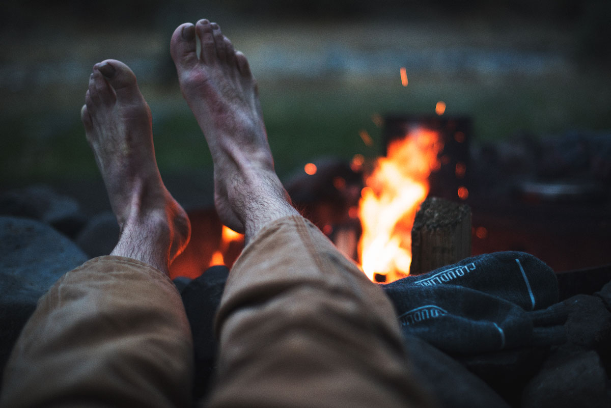 Hiker drying bare feet and wet socks next to campfire.