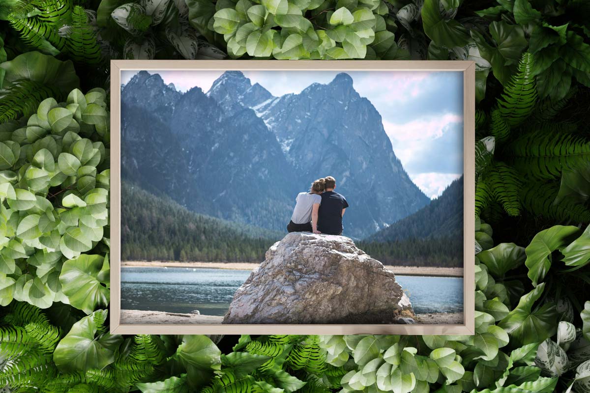 framed photo of couple sitting on rock in front of backcountry lake with mountains in the background.