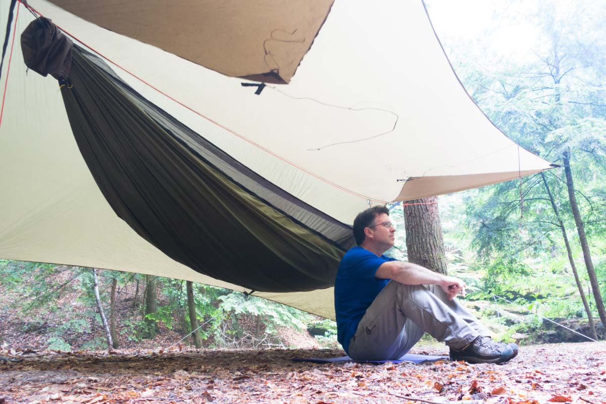 Camper sitting on the ground under a hammock tarp and hammock.