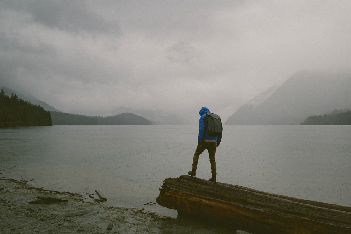 Hiker standing on large log on lake shore under stormy ski.