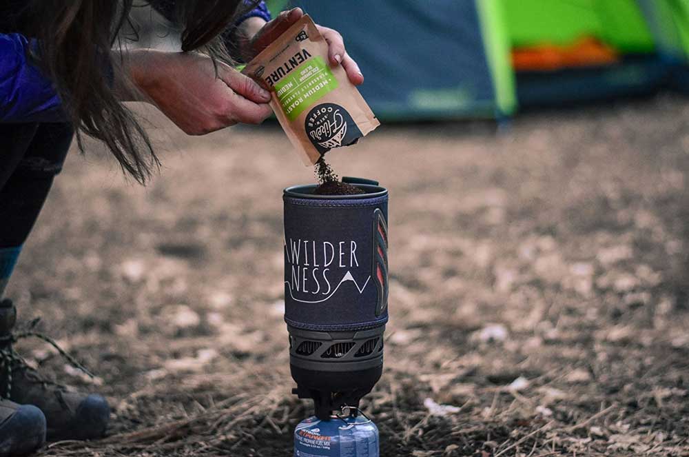 Camper pouring a hiker brew pouch into a backpacking stove pot.