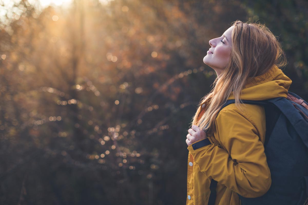 Hiker standing still on a trail and breathing in deep while putting their face to the sun.