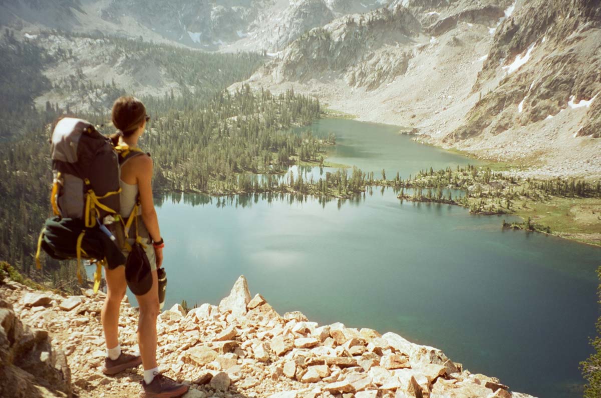 Female backpacker on hiking trail overlooking backcountry lake.