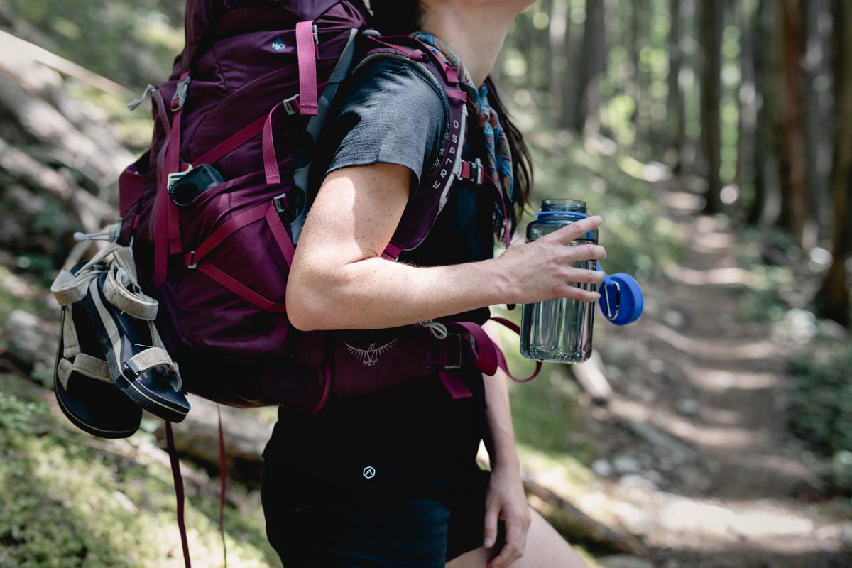 Close up of backpacker showing backpack adjusted for proper fit while holding an open water bottle.