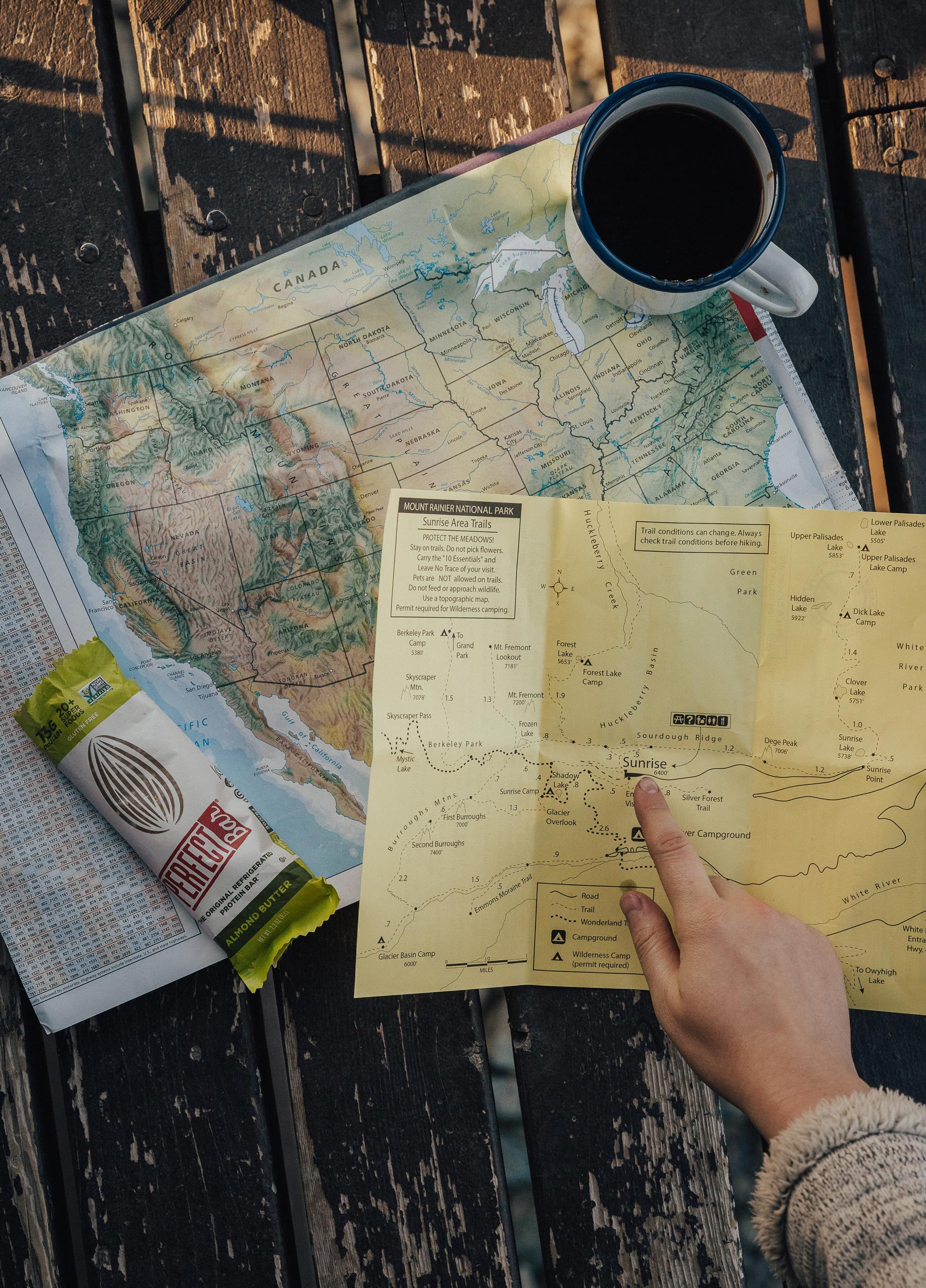 Hiker studying trail maps with morning coffee.