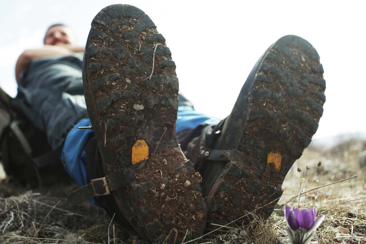 Hiker taking a break on the trail wearing merino wool socks, waterproof boots, and gaiters to keep feet dry.