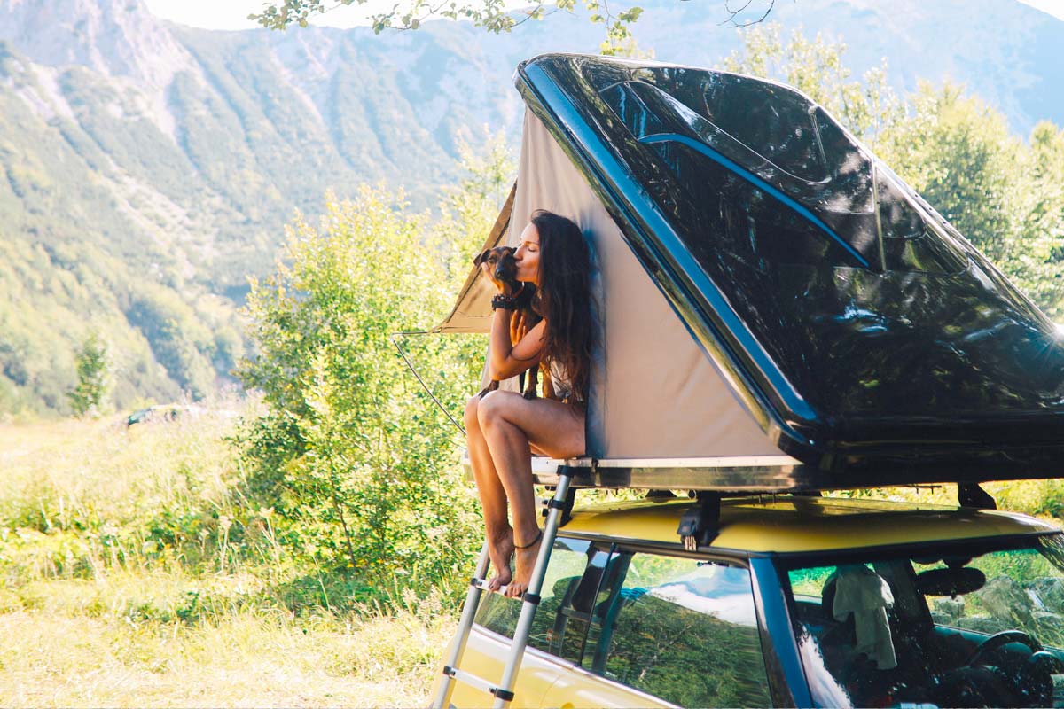 Women holding dog while sitting in rooftop tent.