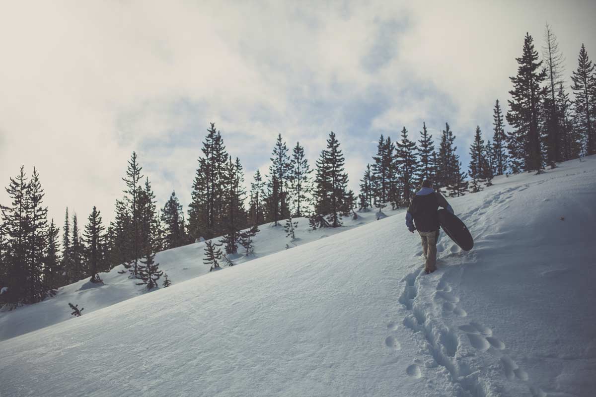 Winter adventure: Man treks uphill with inner tube for snowy sledding.