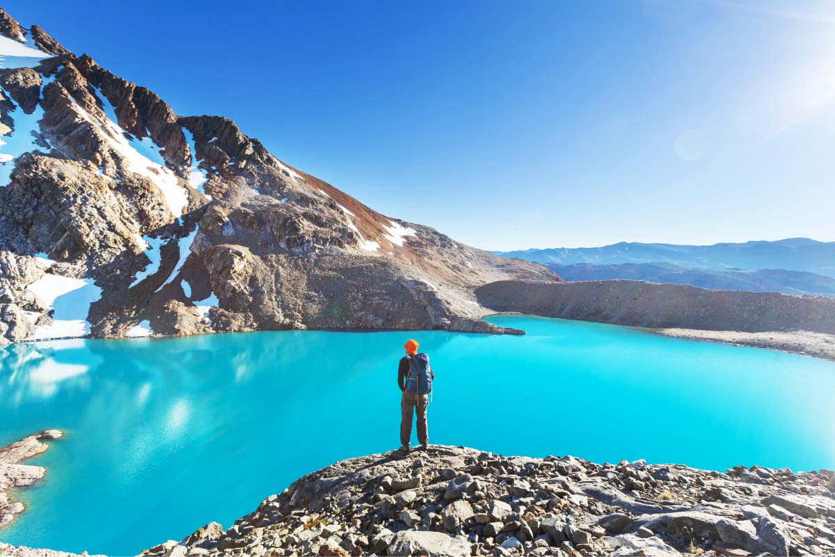 Hiker facing a blue mountain lake wearing sun protective clothing.