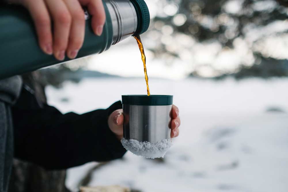 Hiker pouring coffee from a thermos on a snowy trail.