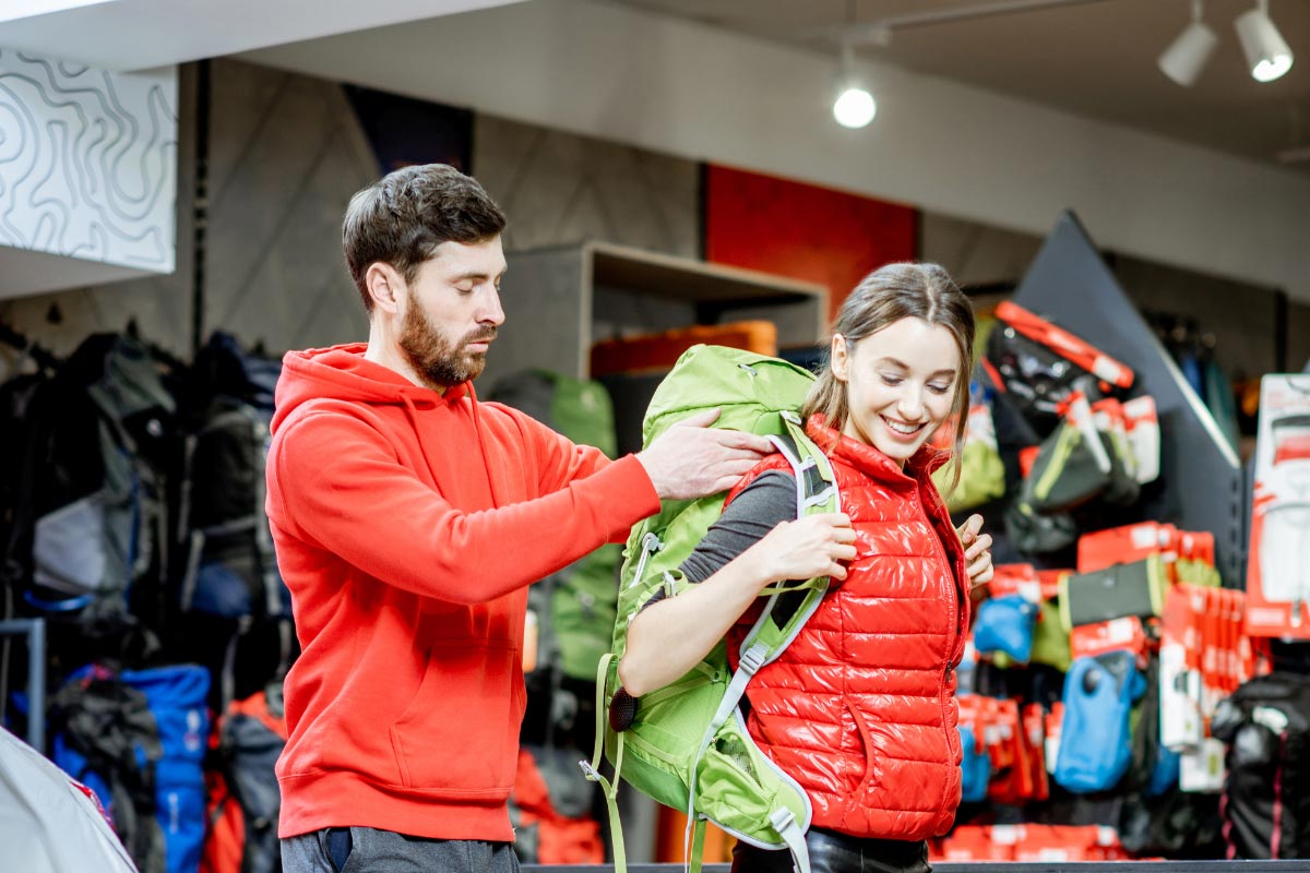 Man helping woman try on a backpack for fit in a store.