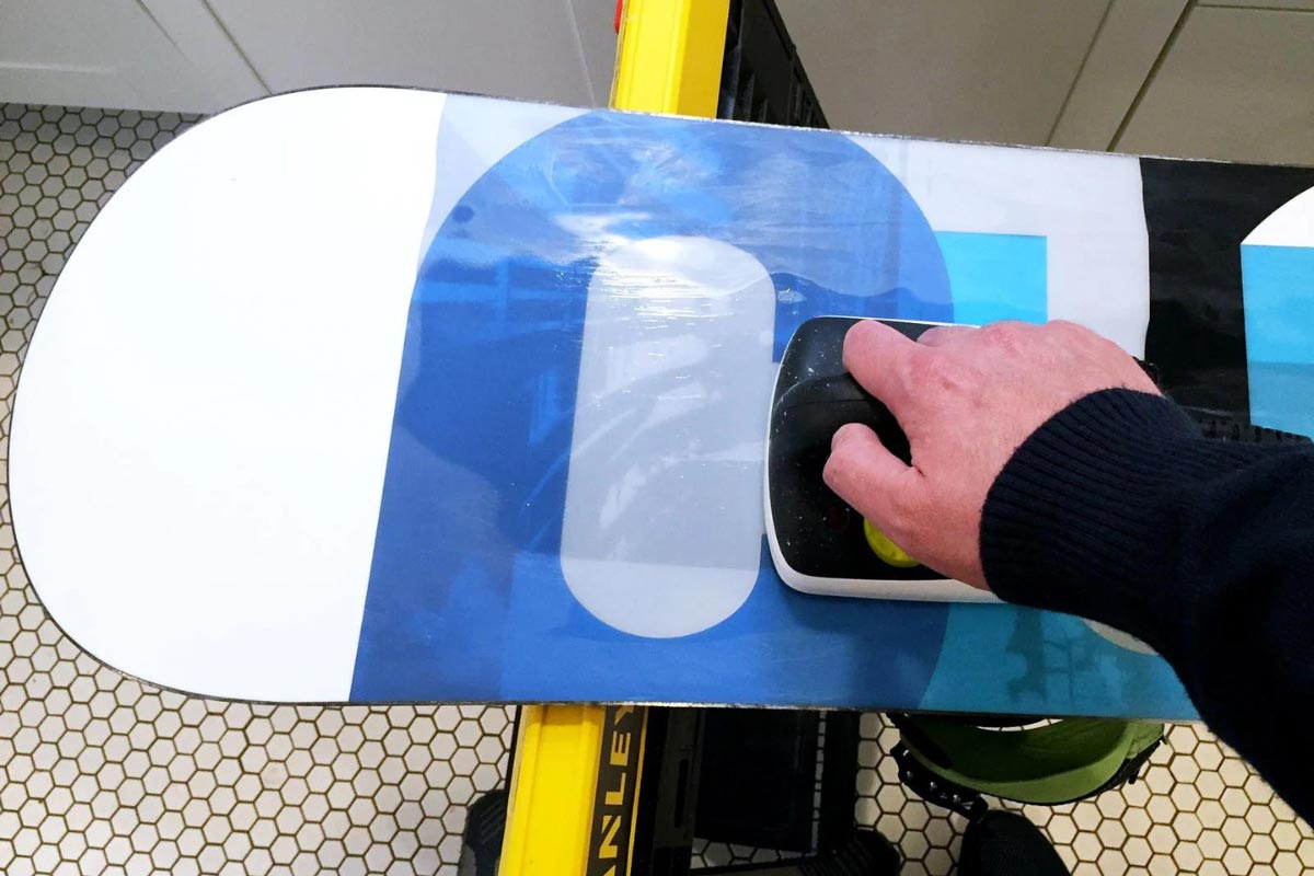 Person running wax iron back across wax covered snowboard base.