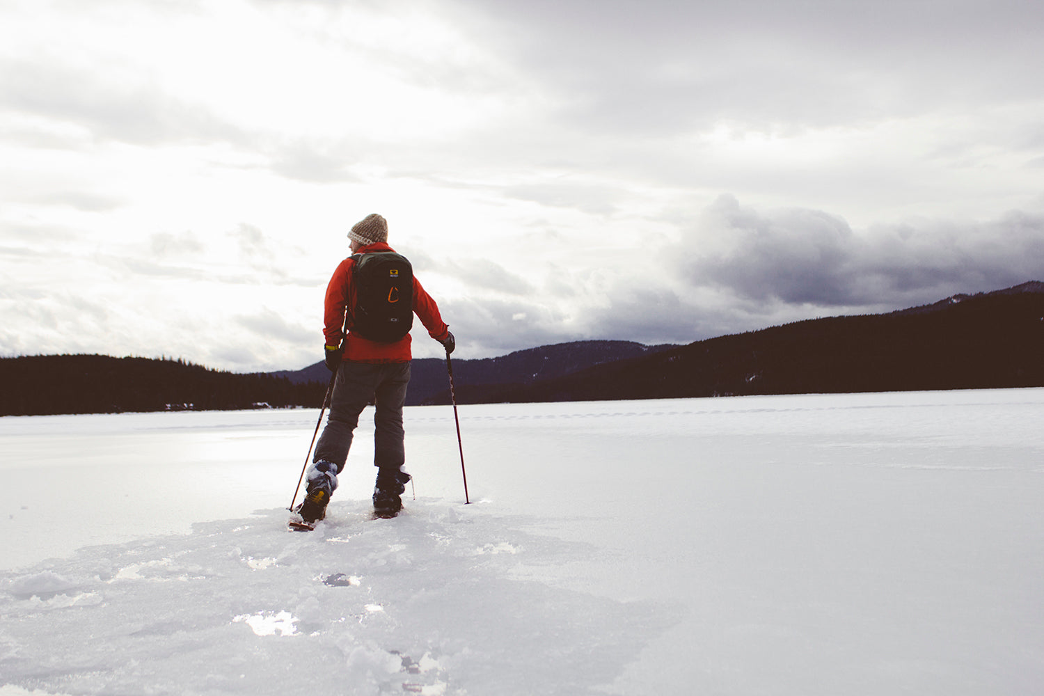 Snowshoer adventuring across deep snow on a frozen mountain lake.