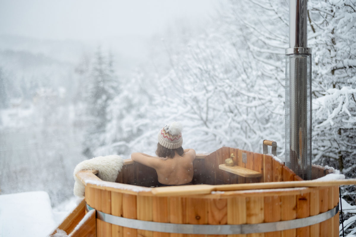 Women relaxing in a wood stove hotub with snowy trees in the background.