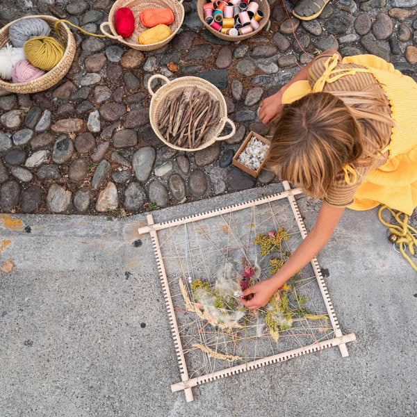 Little girl playing with gathered treasures and Grapat weaving frame.