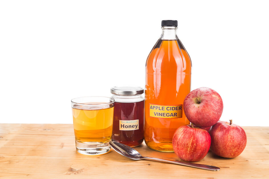 Bottle of apple cider vinegar with honey, apples and a glass with spoon