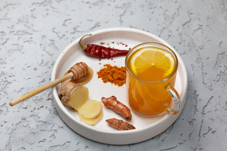Ceramic tray with sliced ginger, honey, cayenne pepper and a glass with a brown liquid and a slice of lemon