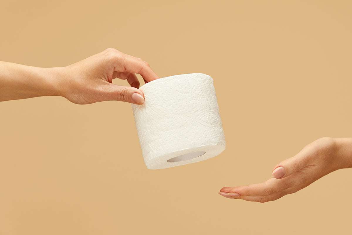 A roll of toilet paper being handed from one hand to another