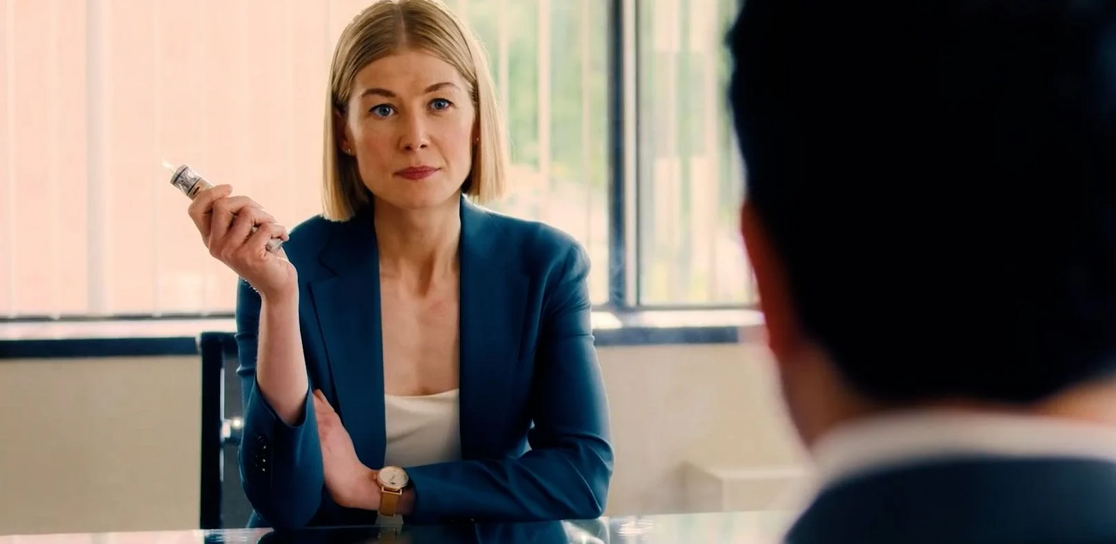 A still from the film "I Care A Lot", where a woman at a desk holds a vape.