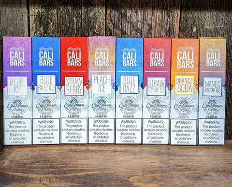 Several boxed disposable vapes set in a line across a wooden backdrop.