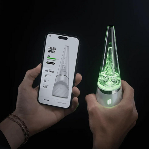 One hand holding the Puffco Peak Pro product, while the other hand holds a smartphone displaying the interface of the app used to control the Puffco Peak Pro.