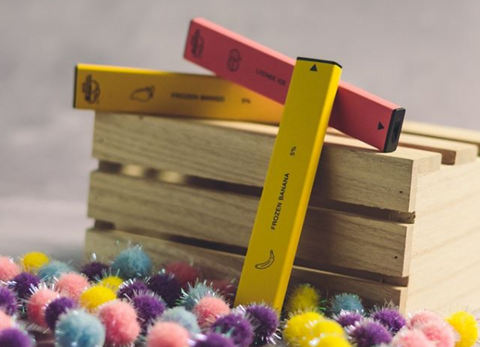 Three disposable vapes laying atop a wooden crate with colorful balls surrounding them.