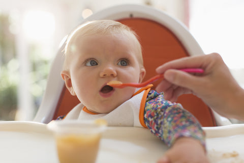 Baby in high chair eating baby food.
