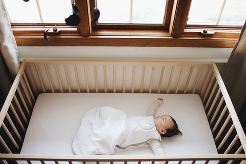 Baby sleeping in crib dressed in baby sleep sack.