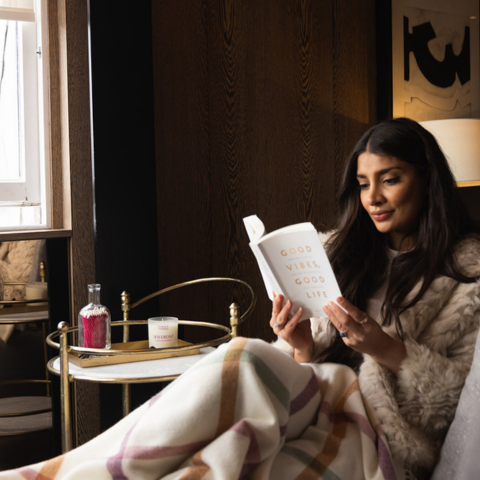 woman wrapped in a blanket reading a book with a black pomegranate candle burning in the background