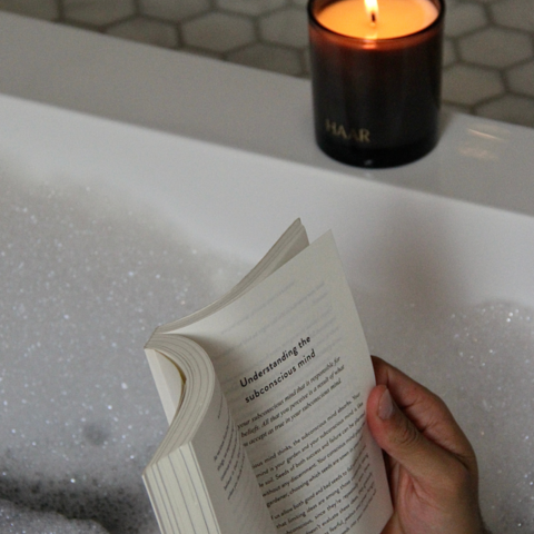 Close up of someone reading in the bath next to a candle