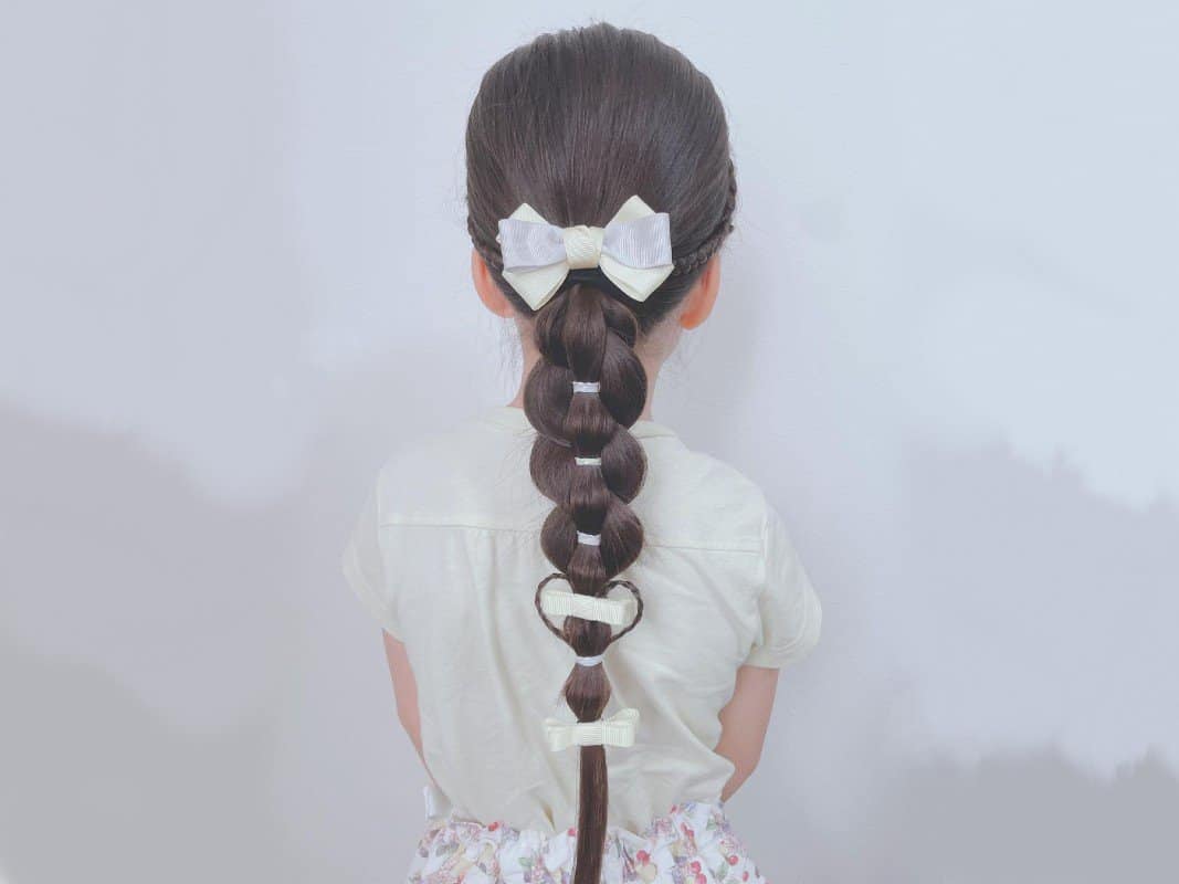 girl with brown French sleek braided ponytail with bows