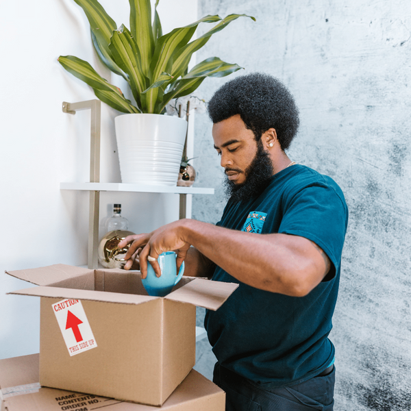 Black male in dark green shirt placing a teal mug in a cardboard box