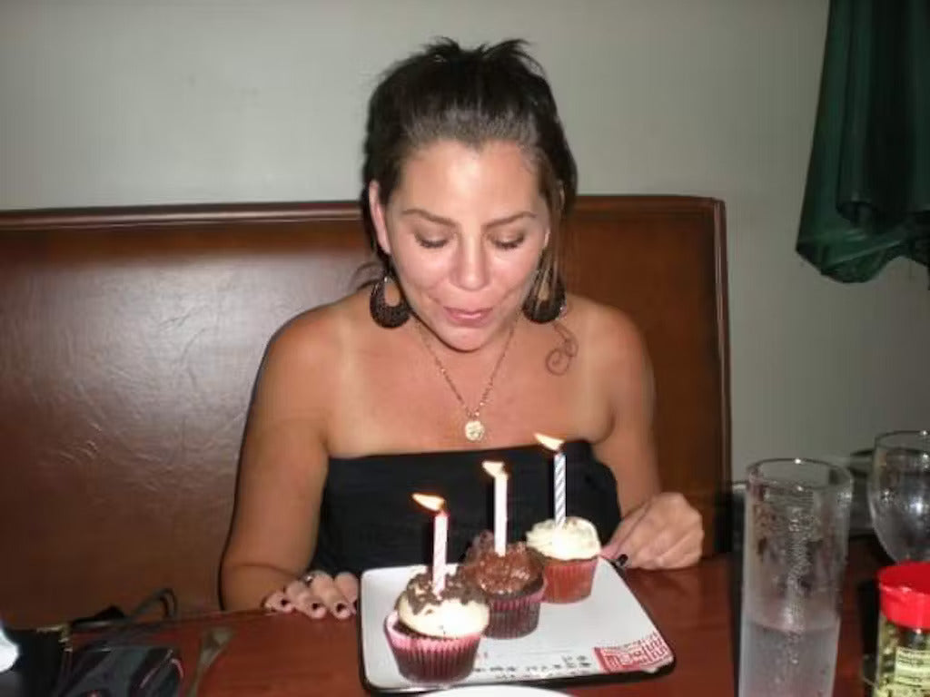 Woman celebrating with two cupcakes with lit candles.