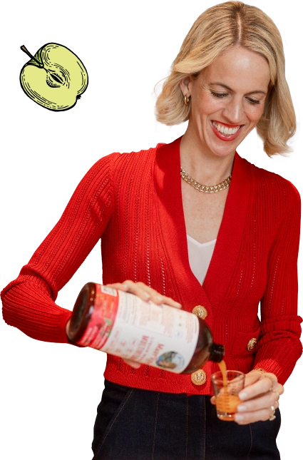 Woman in a red sweater pouring liquid from a bottle into a small cup.