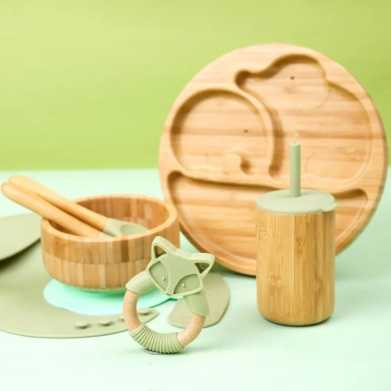 Set of bamboo baby utensils and teething ring on a light green background