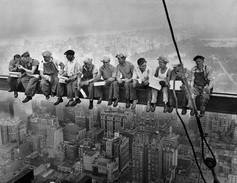 A row of construction workers sit on a girder suspended high above New York City.