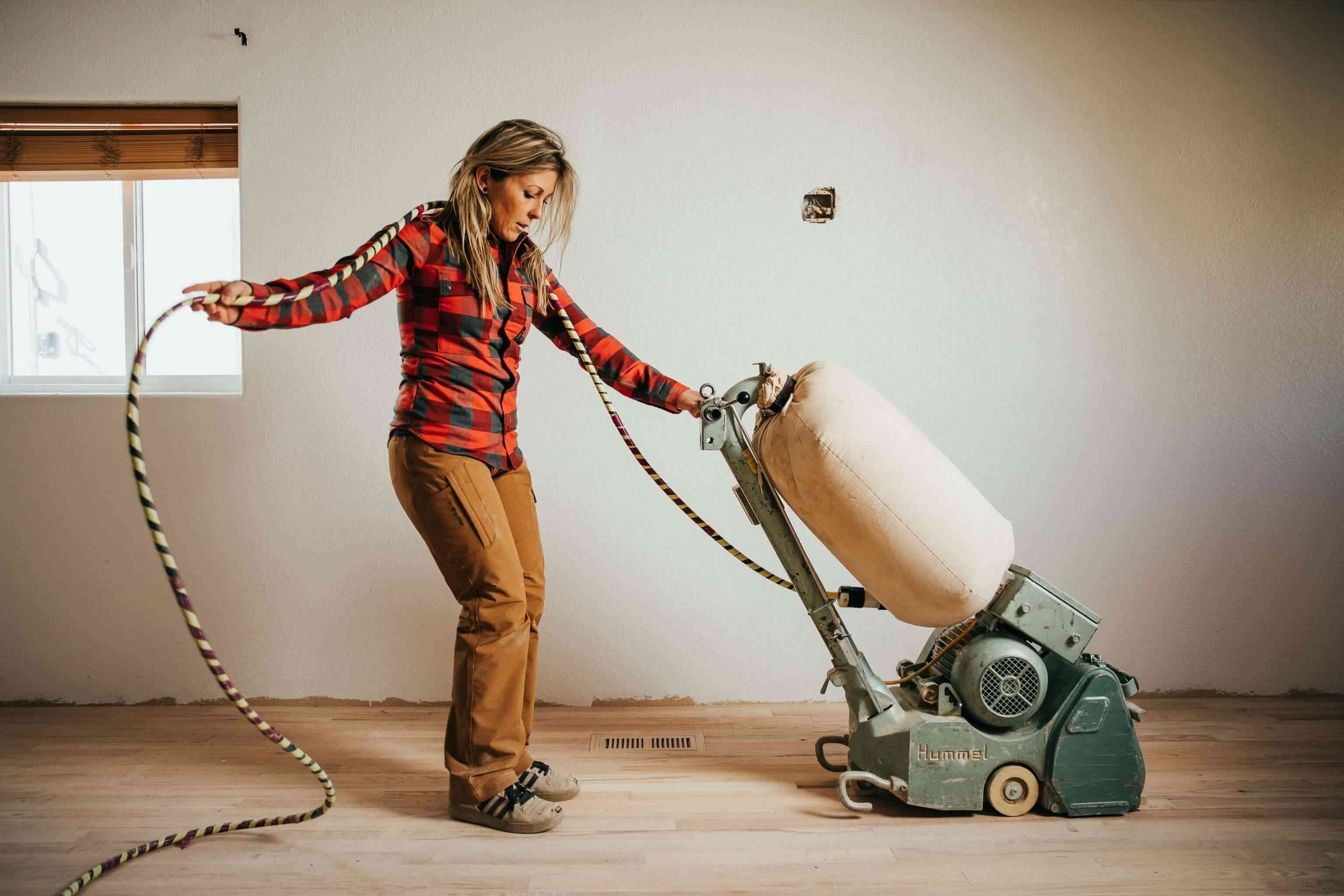 Laurie Bitzkowksi maneja una lijadora de pisos mientras trabaja en un piso de madera en la remodelación de una casa.