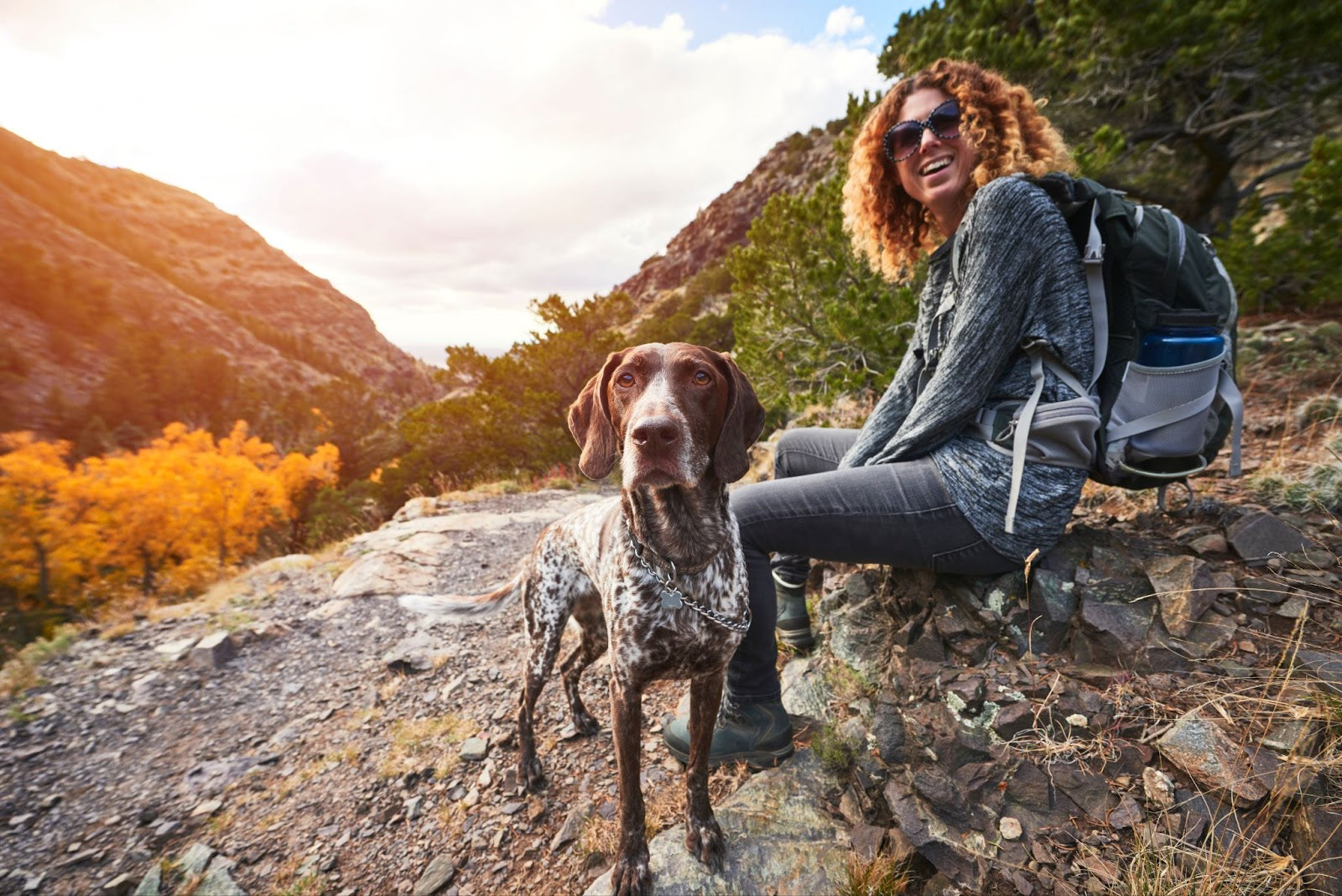 Woman backpacking with her dog, sitting on a rock during outdoor adventure