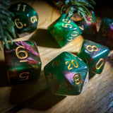 A photo of the dice set Titania from D20Collective. The dice are a shimmering, swirling green and pinkish-red, set against a light wooden background