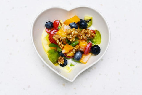 A photo of a bowl of yoghurt and fruit in the shape of a heart against a white background