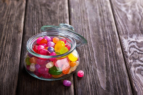 A photo of a clear jar full of boiled candies on top of a dark wooden surface