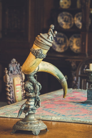 Photo of an antique-looking desk, with a drinking horn set on a stand in focus in the front of the photo
