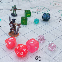 A photo of two DnD miniatures on a batttle mat. The minis are surrounded by various die, which are pink, blue, and purple. The dice are set within the squares of the mat, not as though they have been rolled, but as if they are additional miniatures