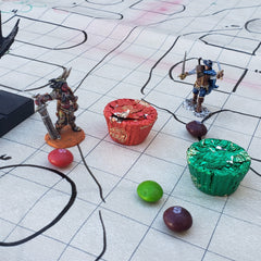 A photo of several DnD minis on a battlemap. The miniatures are interspersed with a couple of Reese's Cups and Skittles, as though the candies are additional miniatures