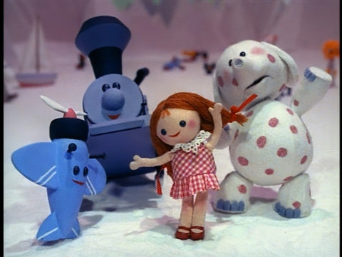 A photograph of the dolls and toys from the Island of Misfit Toys in Rudolph the Rednosed Reindeer. There is a small redheaded doll in a polkadot dress, a polkadot elephant, a blue train, and a blue airplane. 