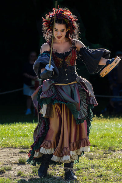 A photo of a woman at the New York Renaissance Festival. She wears a colorful 'wench' style dress, and is lunging forward with a rapier. 