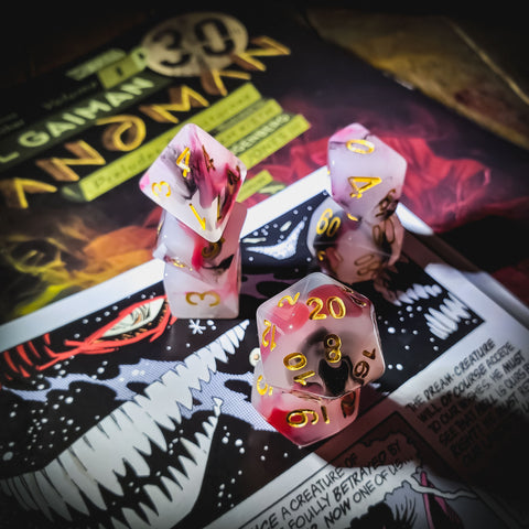 A photo of s set of gaming dice in red, white, and black swirls with gold numbers. The dice are stacked on an old gaming magazine.