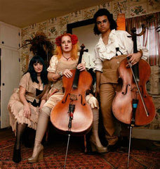 A photo of the band Rasputina. There are 3 woman, two of whom have callos, wearing period clothing and looking at the camera
